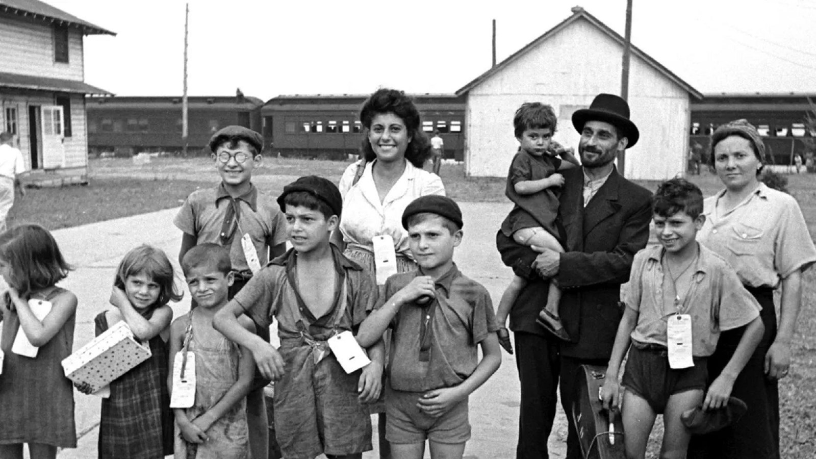 A group of smiling adults and children stand in a courtyard with buildings in the background.