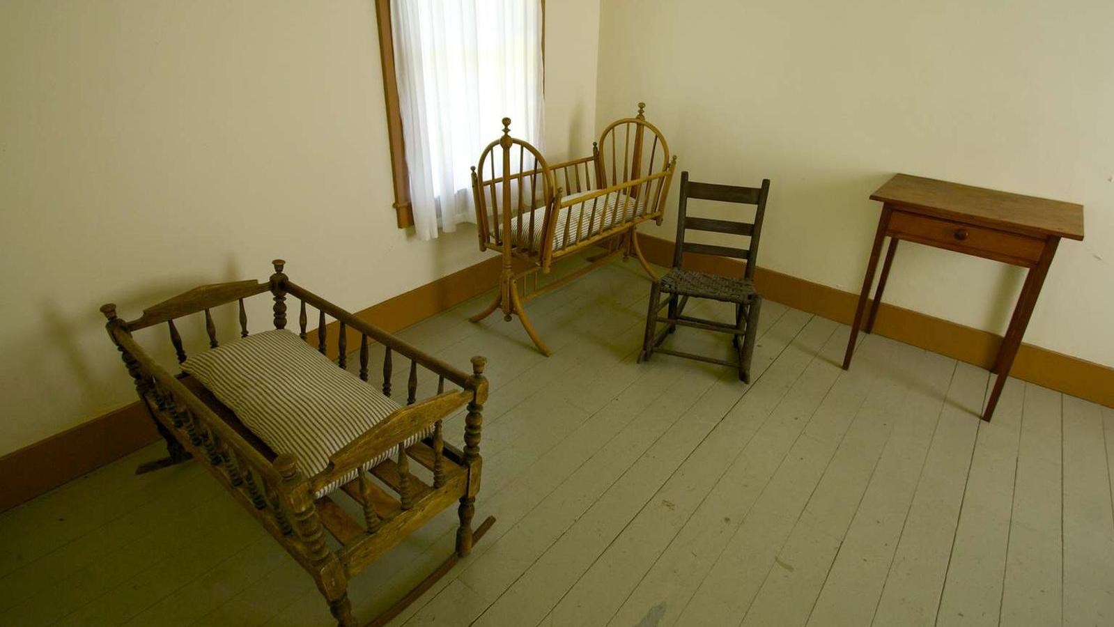 Antique rocking chairs and cradles furnish a small, plain room.