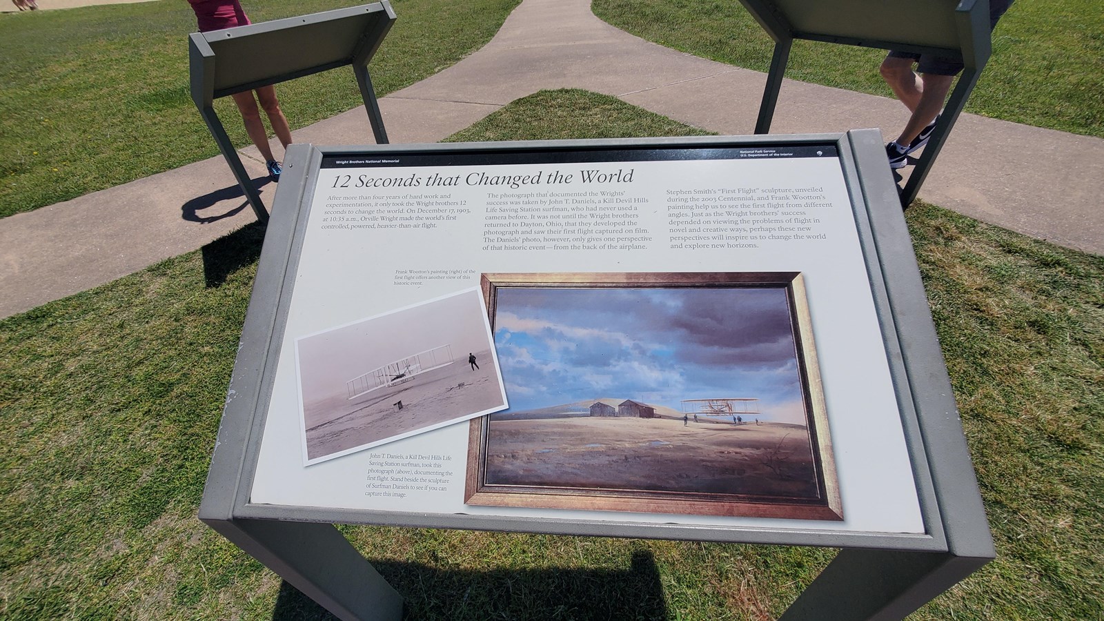 12 Seconds that Changed the World wayside where it sits outside. A paved path can be seen behind it.