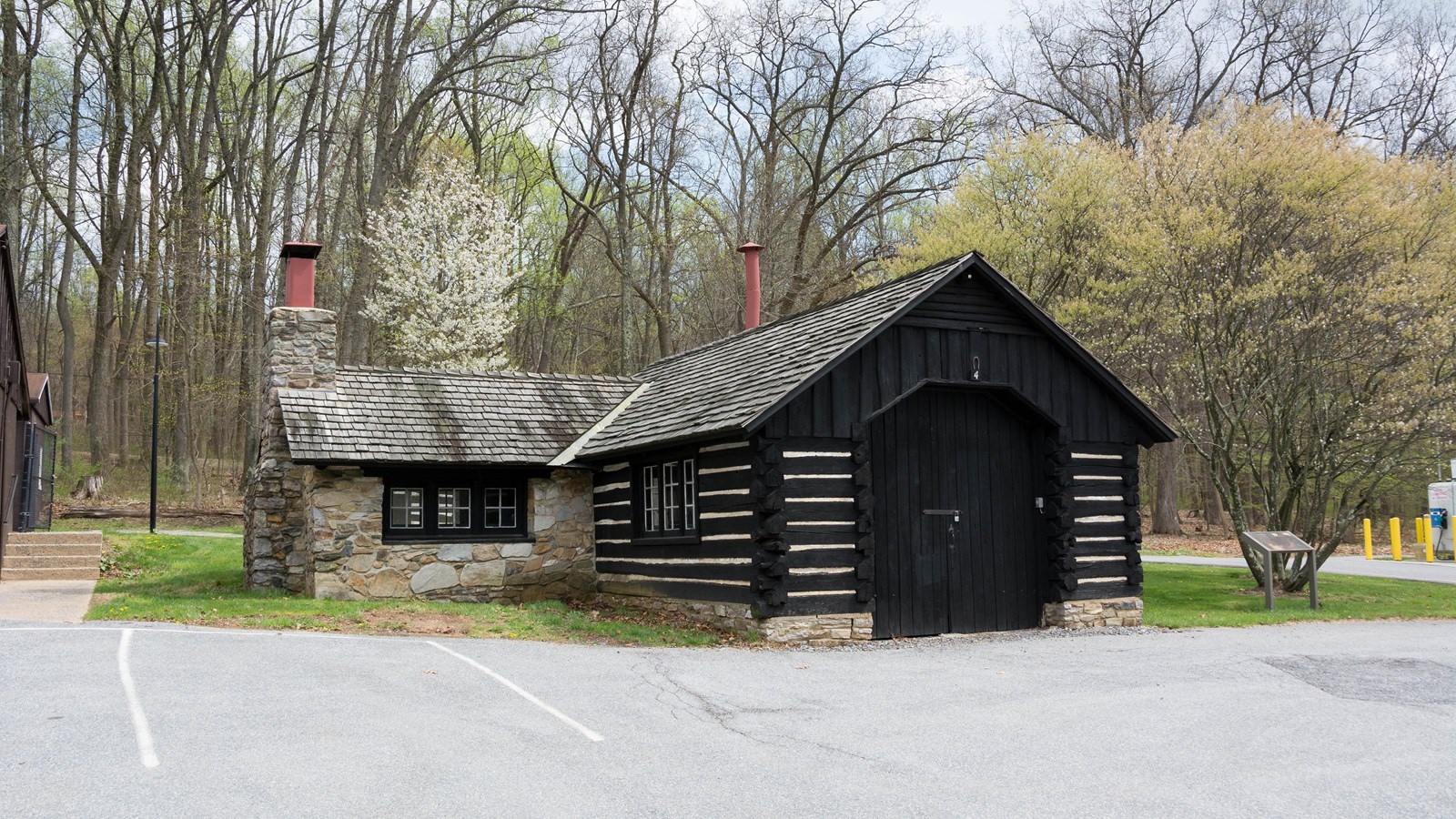 A stone and wooden cabin with red chimney stacks next to a parking lot.