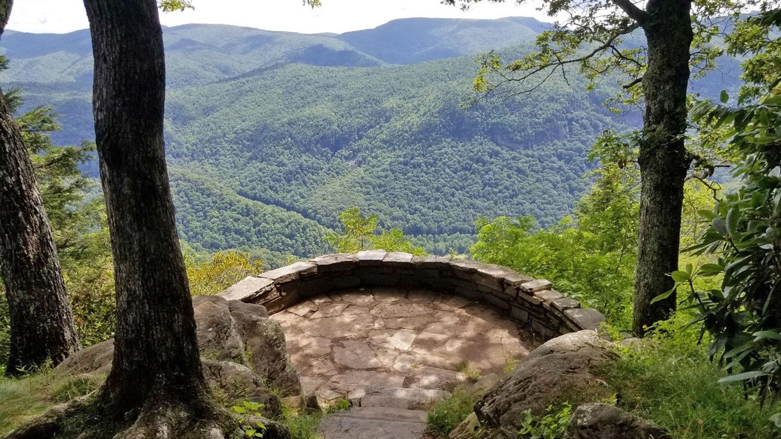 stone steps lead down to a stone platform with a view of green mountains in the distance