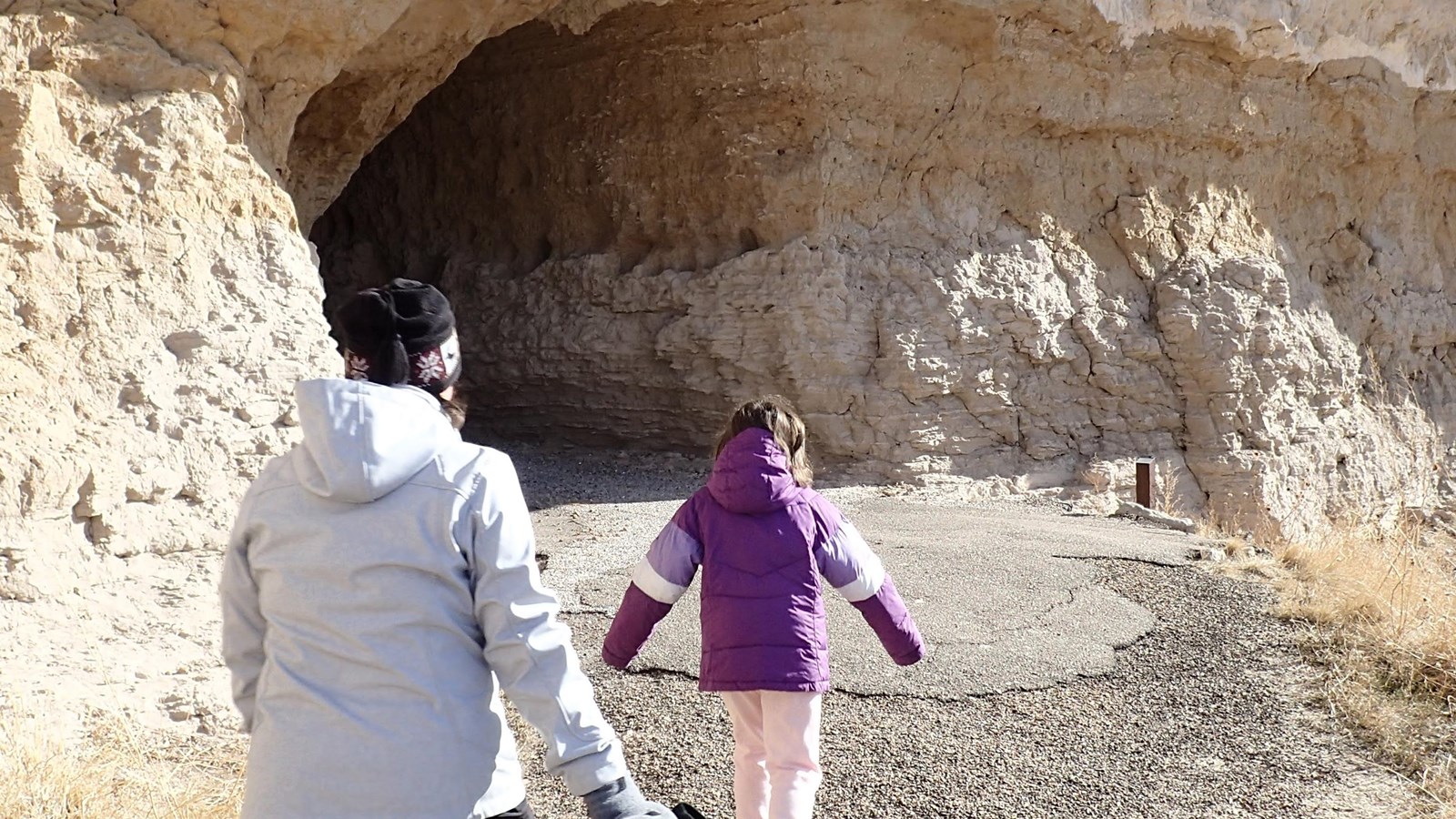 Two hikers approach a tunnel carved into soft sandstone.