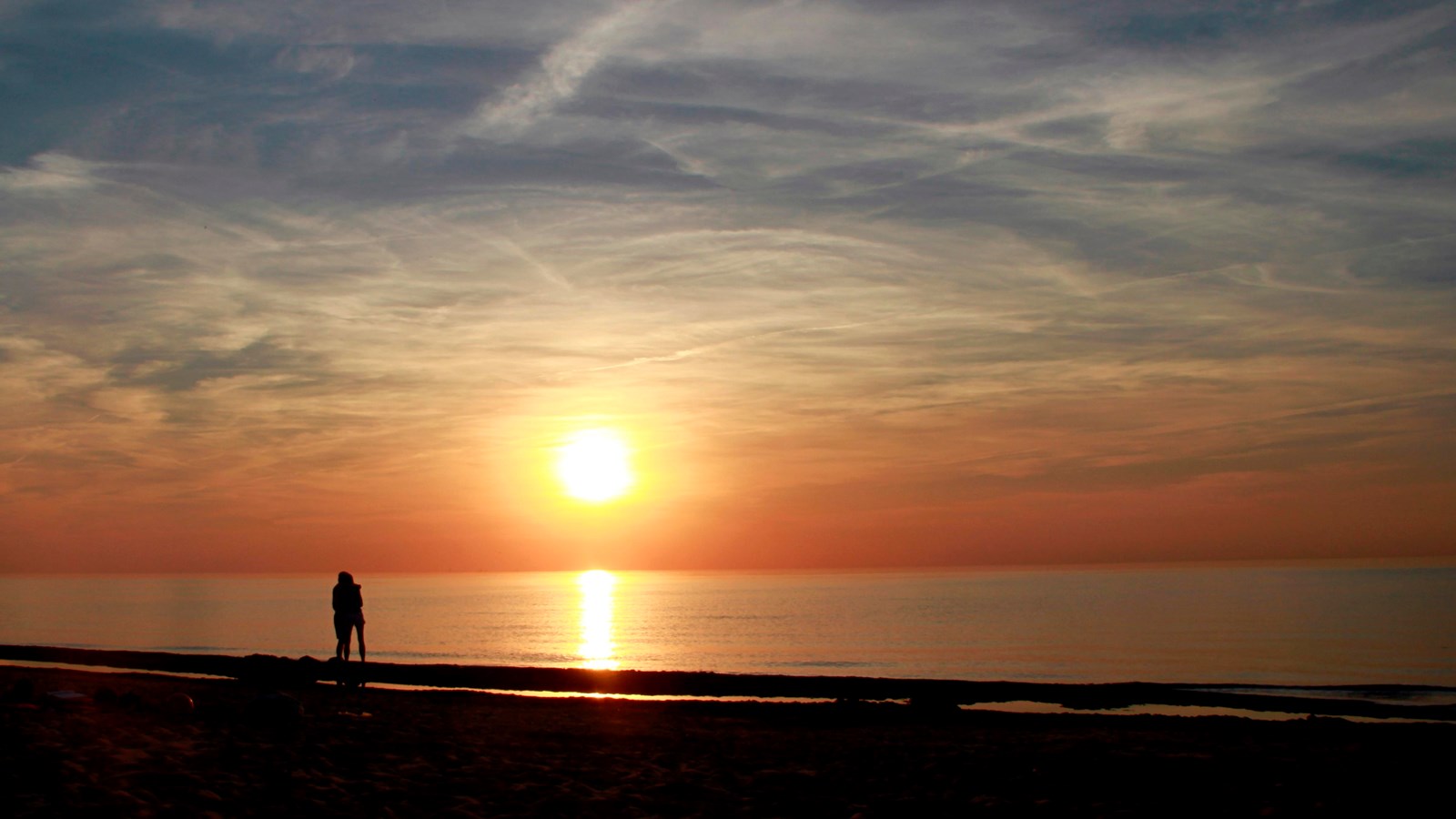 The sun sets along the lake.  A range colors from golds to blue fill the sky.