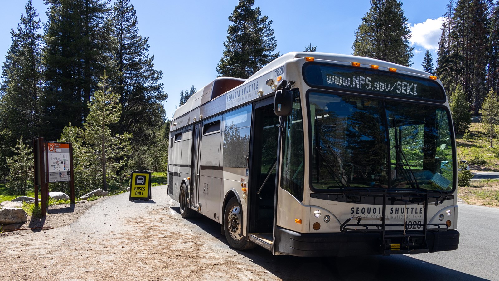 A white shuttle bus is parked next to a sign labeled 