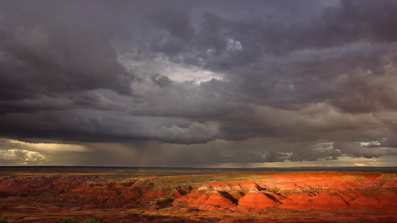 Dark monsoon clouds over the Painted Desert with highlighted badlands.