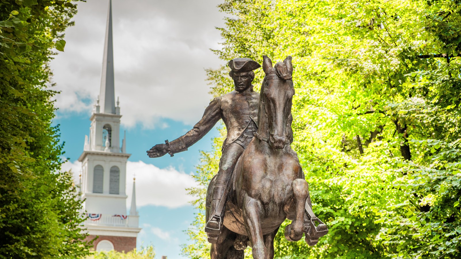 A bronze statue of Paul Revere riding a horse in front of the white steeple of Old North Church
