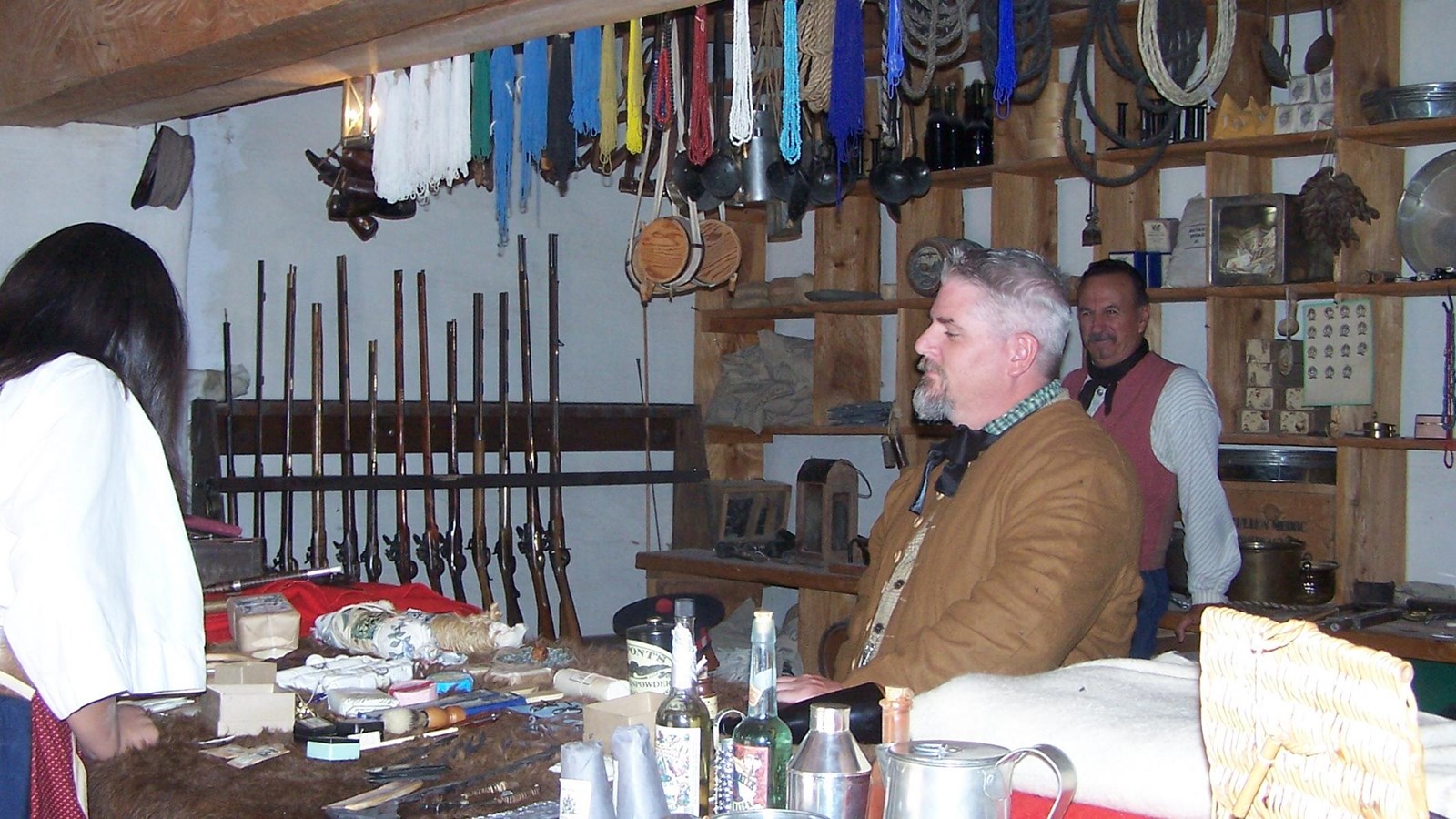 Living historians in a furnished trade room with items displayed on the counter.