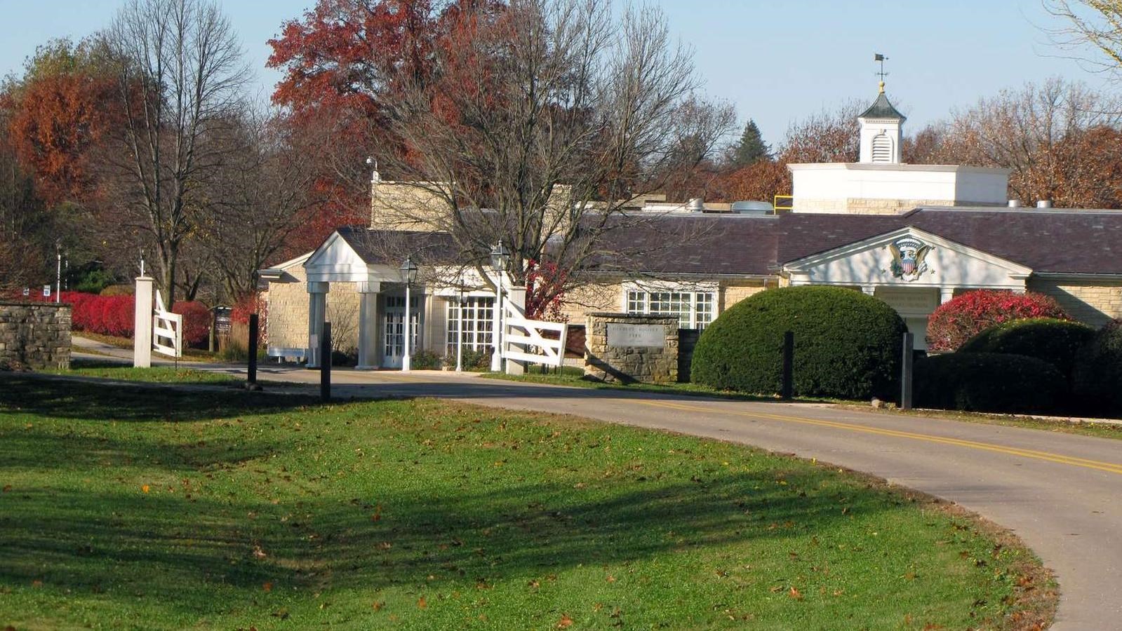 A road is met by a small white gate with stone pillars showing the way to the Presidential Museum an