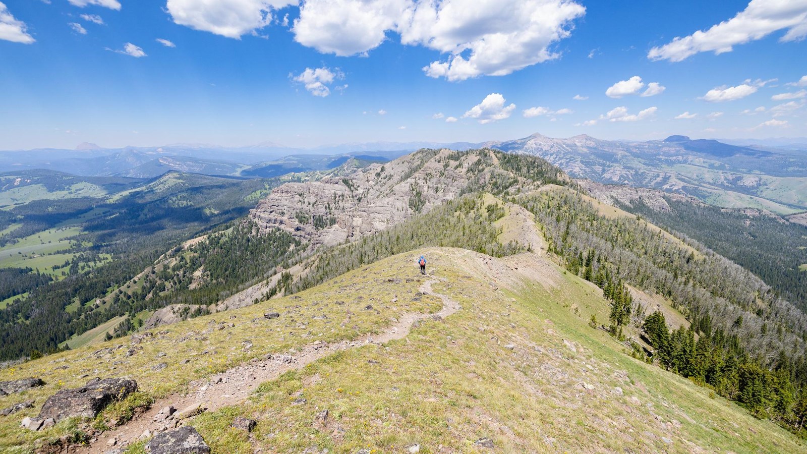 People hike along a trail that traverses a ridgeline.