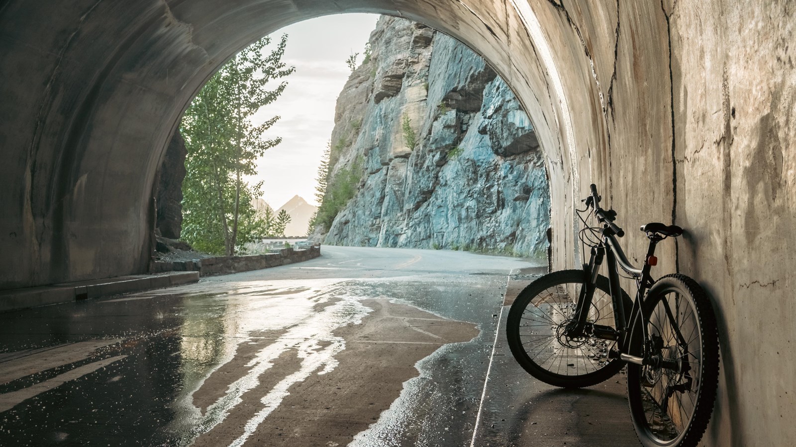 A bike sits inside the west tunnel, which opens to show a road and a distant mountain.