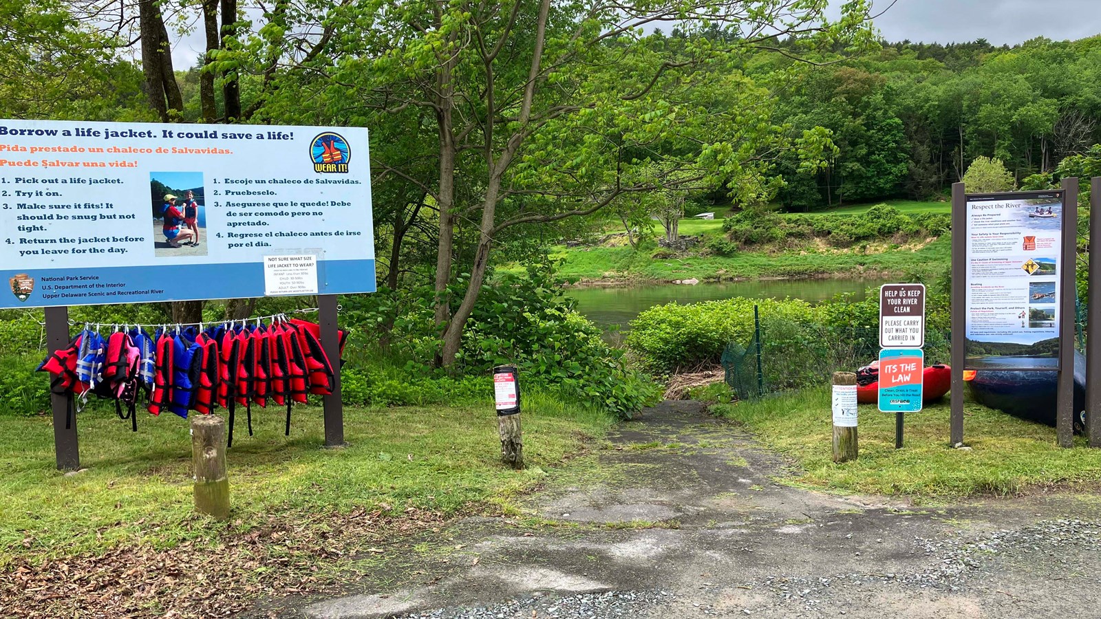 View of gravel path that leads down towards river. On left is life jacket loaner sign.