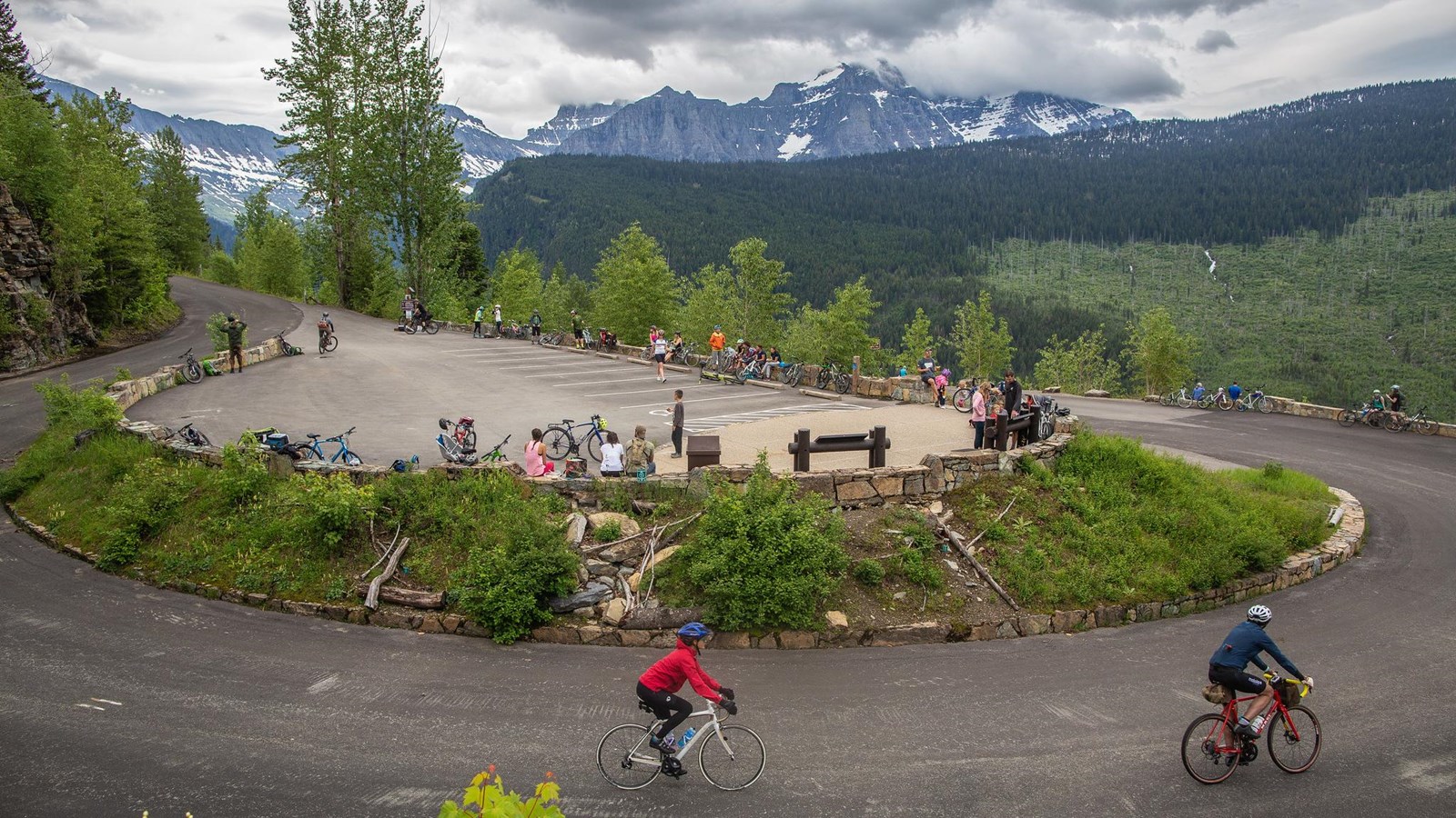 Cyclists riding down a bending road with a parking lot in the center.
