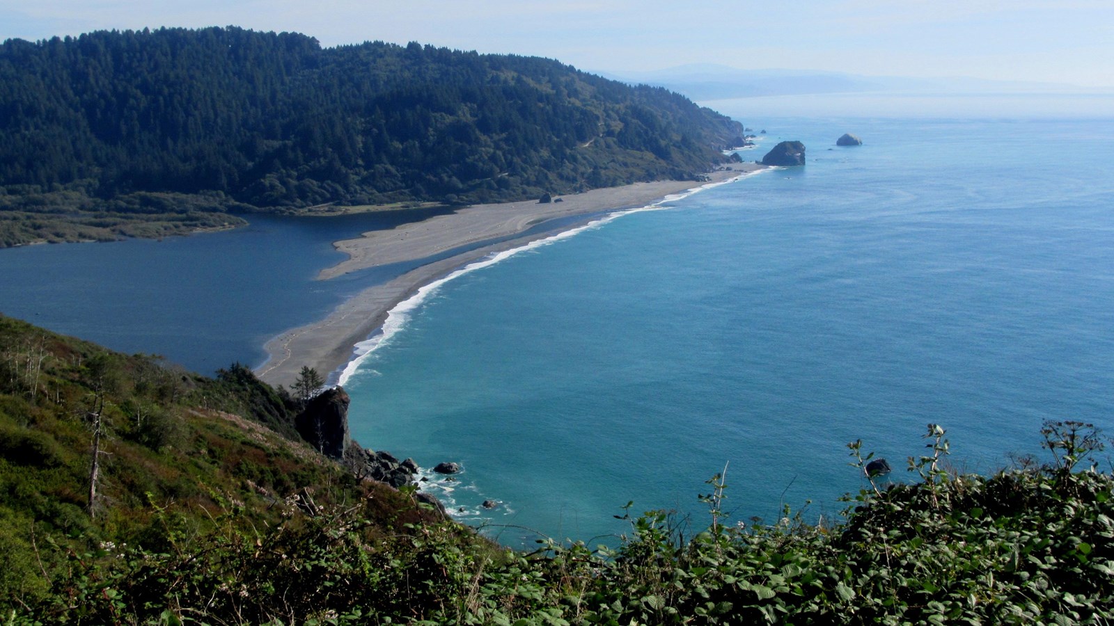 Blue-green ocean and a sandspit at the mouth of a river.