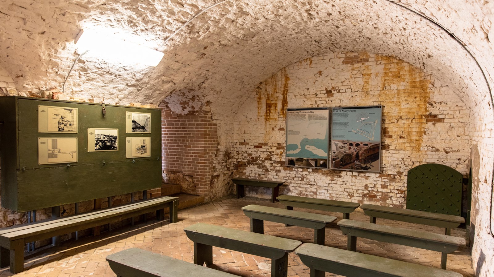 A large green box mounted to the wall and several benches stand under an arched brick ceiling.