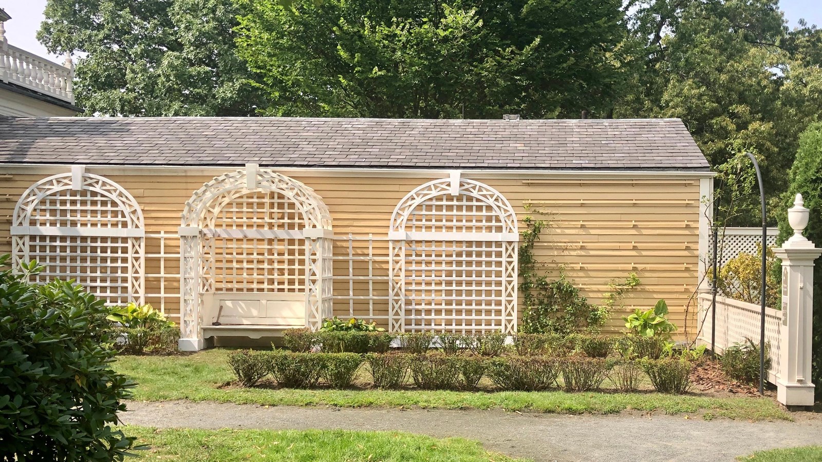 small garden with three white lattice arches along yellow clapboard wall