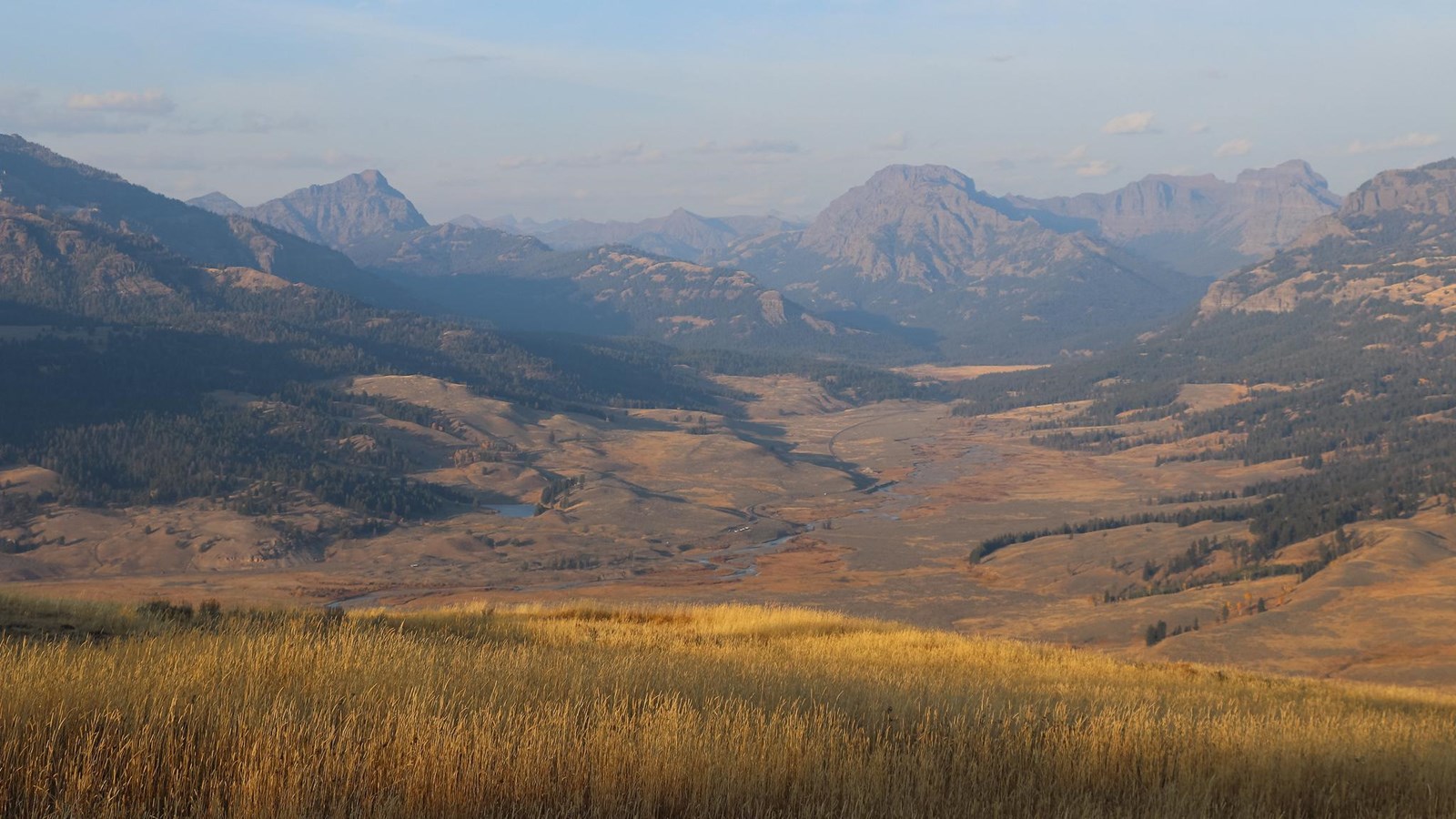 Overlooking a valley with a river running through it and mountains in the distance.