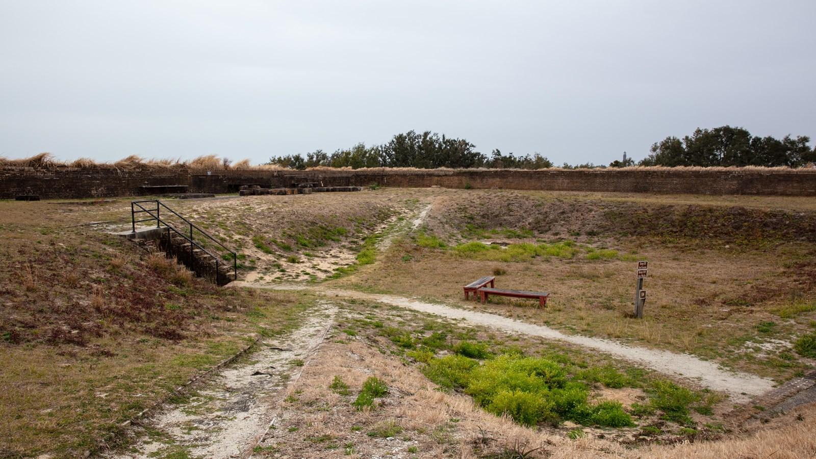 Several dirt ramps lead down to a grassy field with brick walls in the background.