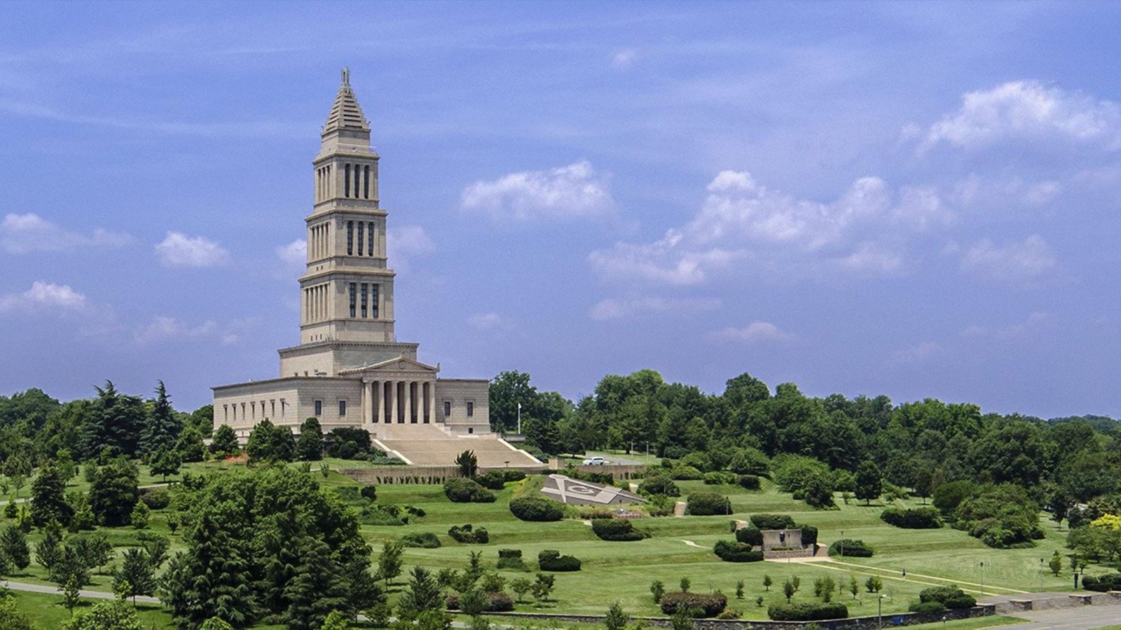 A grand neoclassical building with a tall columnated spire looks out over a large lawn with trees