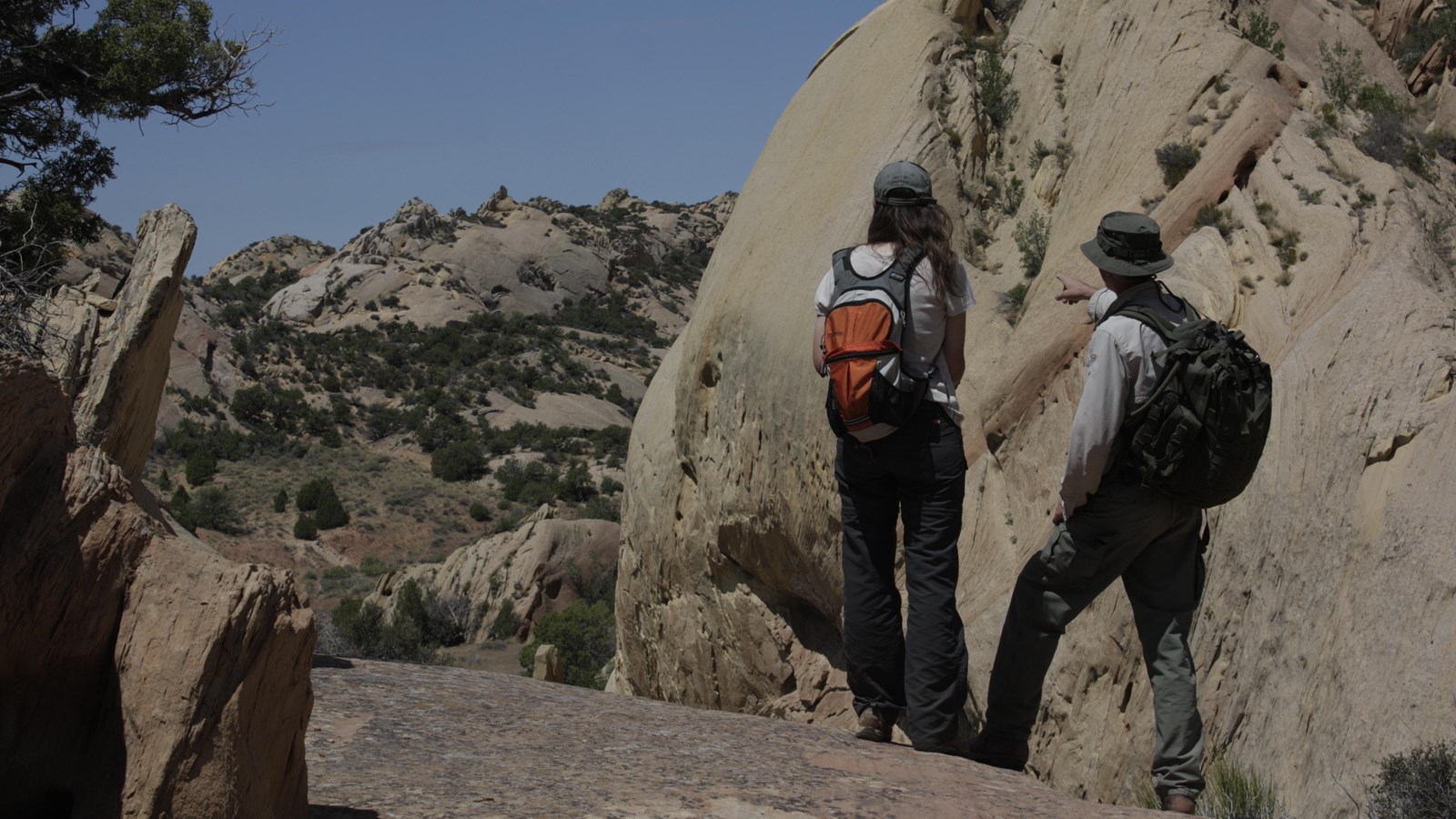 A pair of hikers in a sandstone clearing pointing off into the distance.