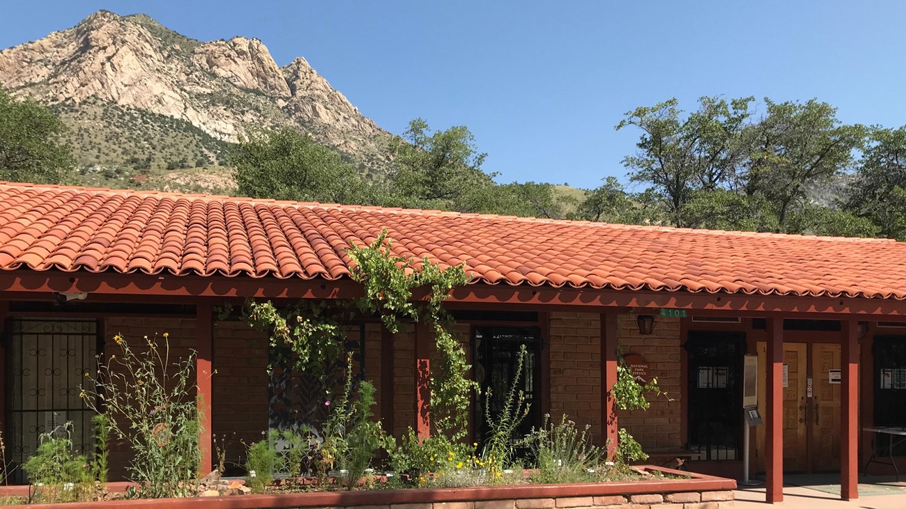 Single story adobe brick building with a red tile roof, Montezuma Peak is visible in the background.