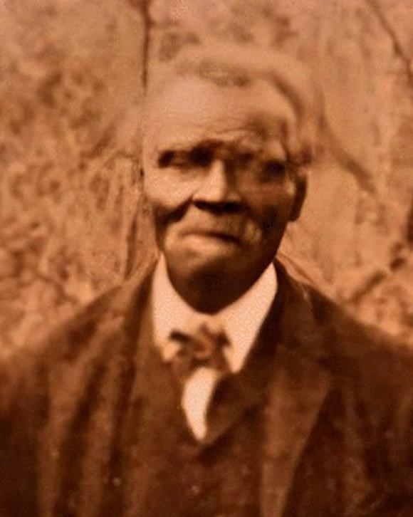 sepia toned photo of Elderly black man with gray hair and mustache stands in black suit and bow tie