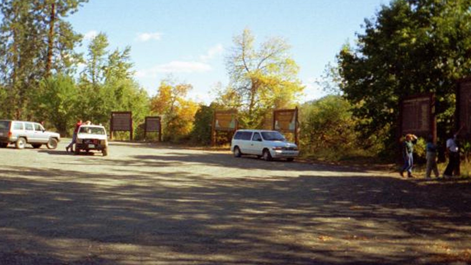 Vehicles parked in a roadside pullout with a gravel lot with information panels 