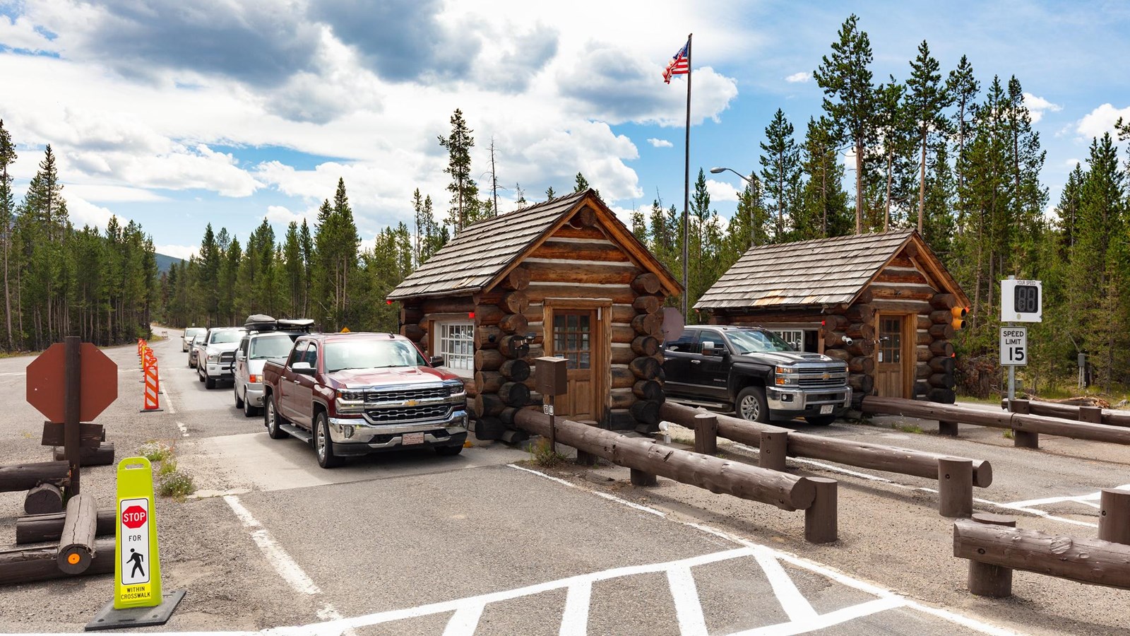 Vehicles travel through an entrance station composed of two, small log cabin buildings.