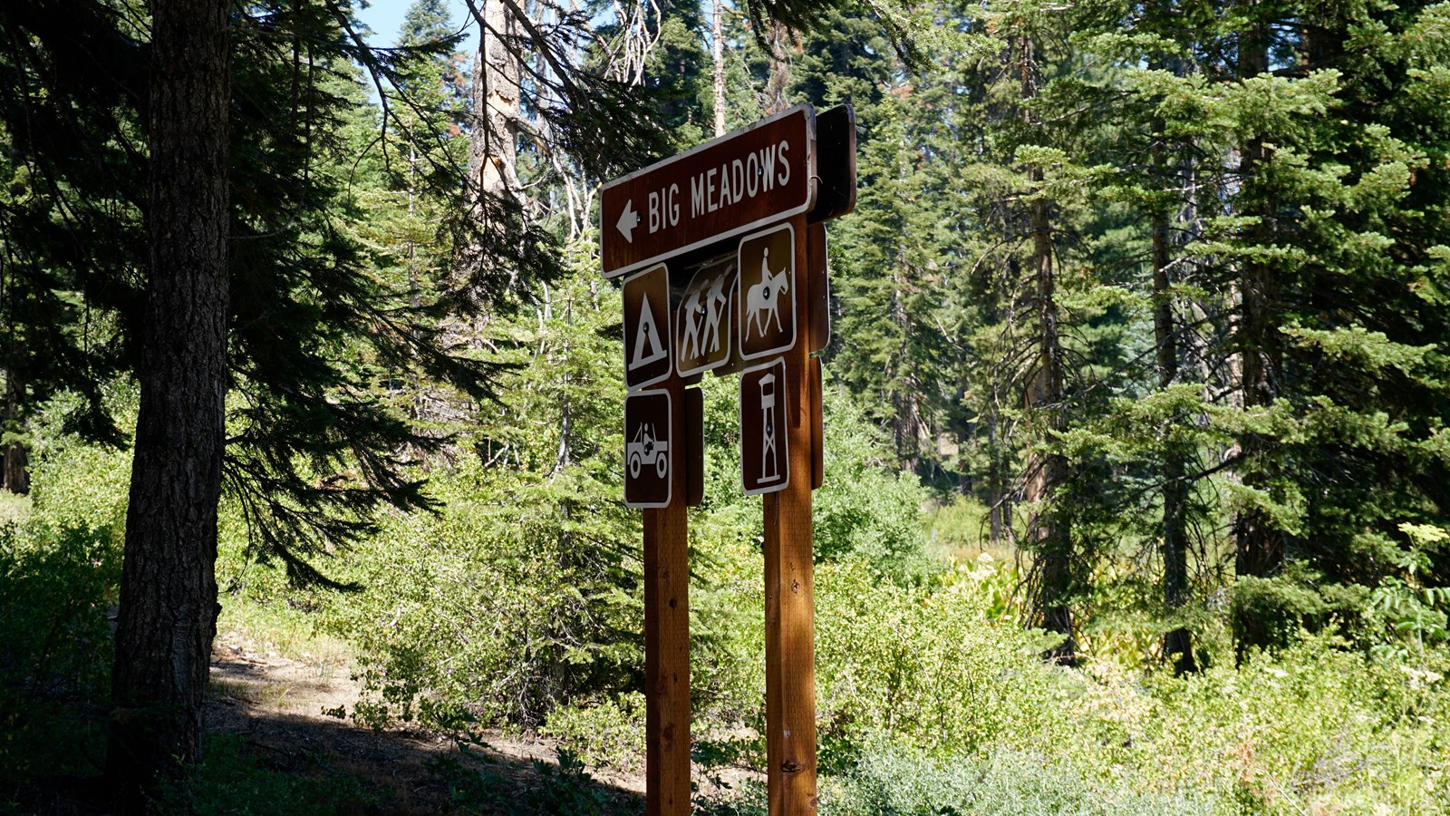 A brown road sign stands in front of green bushes and trees