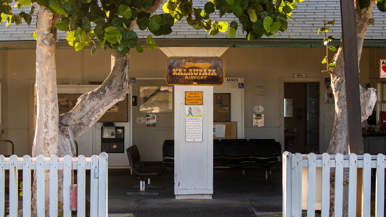 A sign that reads Kalaupapa Airport with a room behind it that is enclosed by walls on three sides.