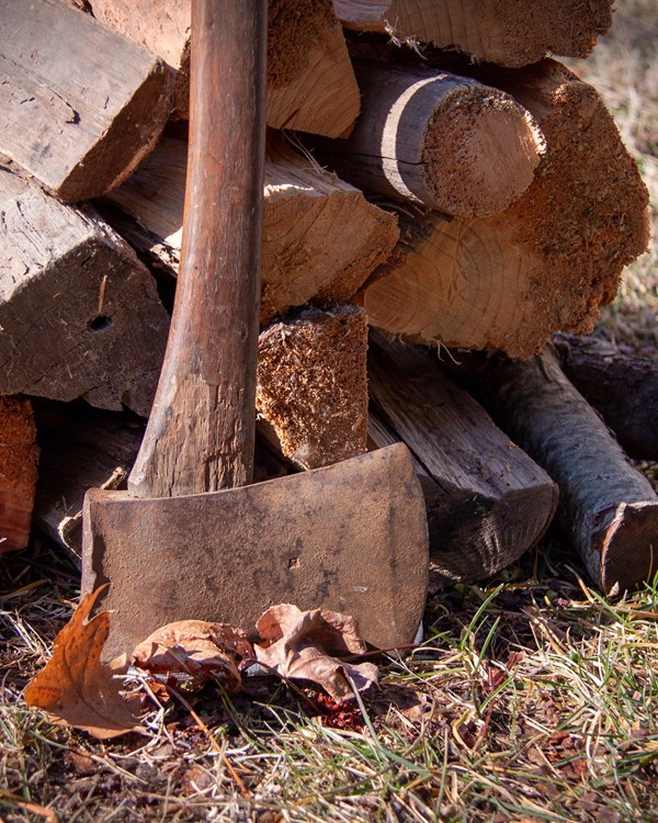 Brown axe with cut firewood in the background. 