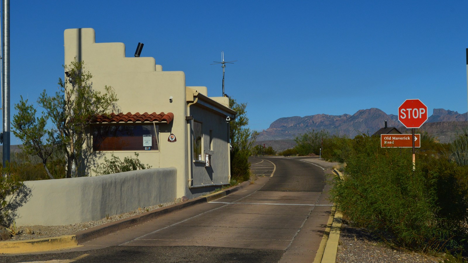 A small adobe building sits between two lanes of highway, with a flagpole and stop sign nearby.