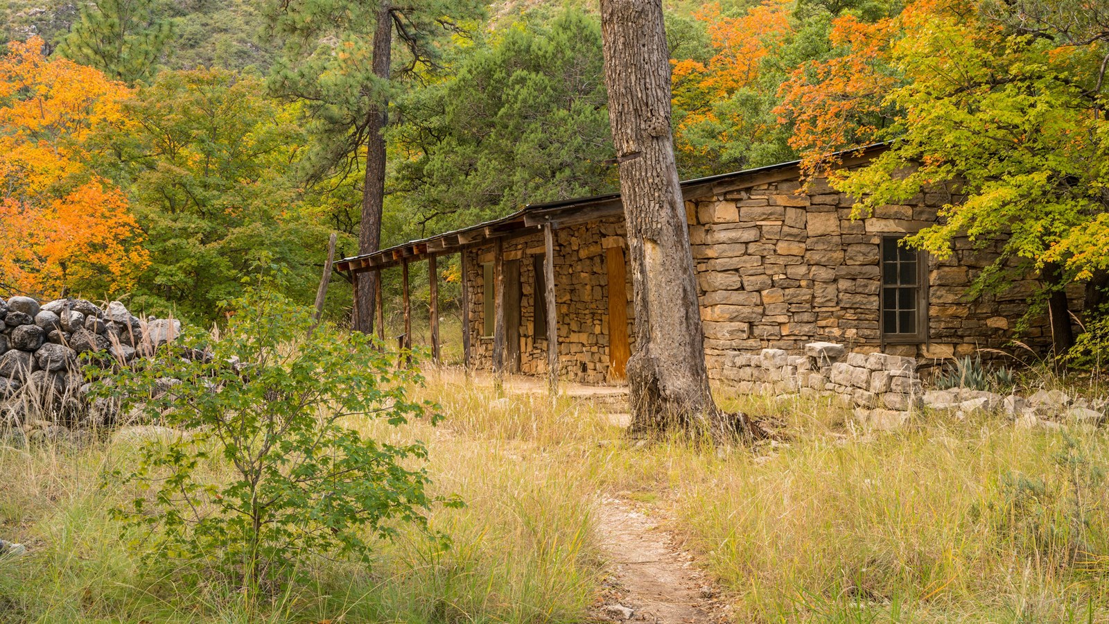 A stone structure in a desert mountain landscape with autumn leaves on the surrounding trees. 