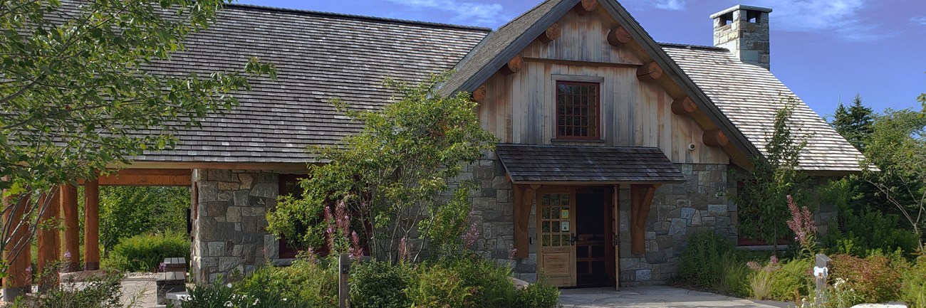 Large, narrow building with stone walls, peeled log columns, cedar shingles, and a stone patio