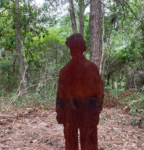 A rust-colored silhouette of a young man. Trees are visible behind the silhouette.