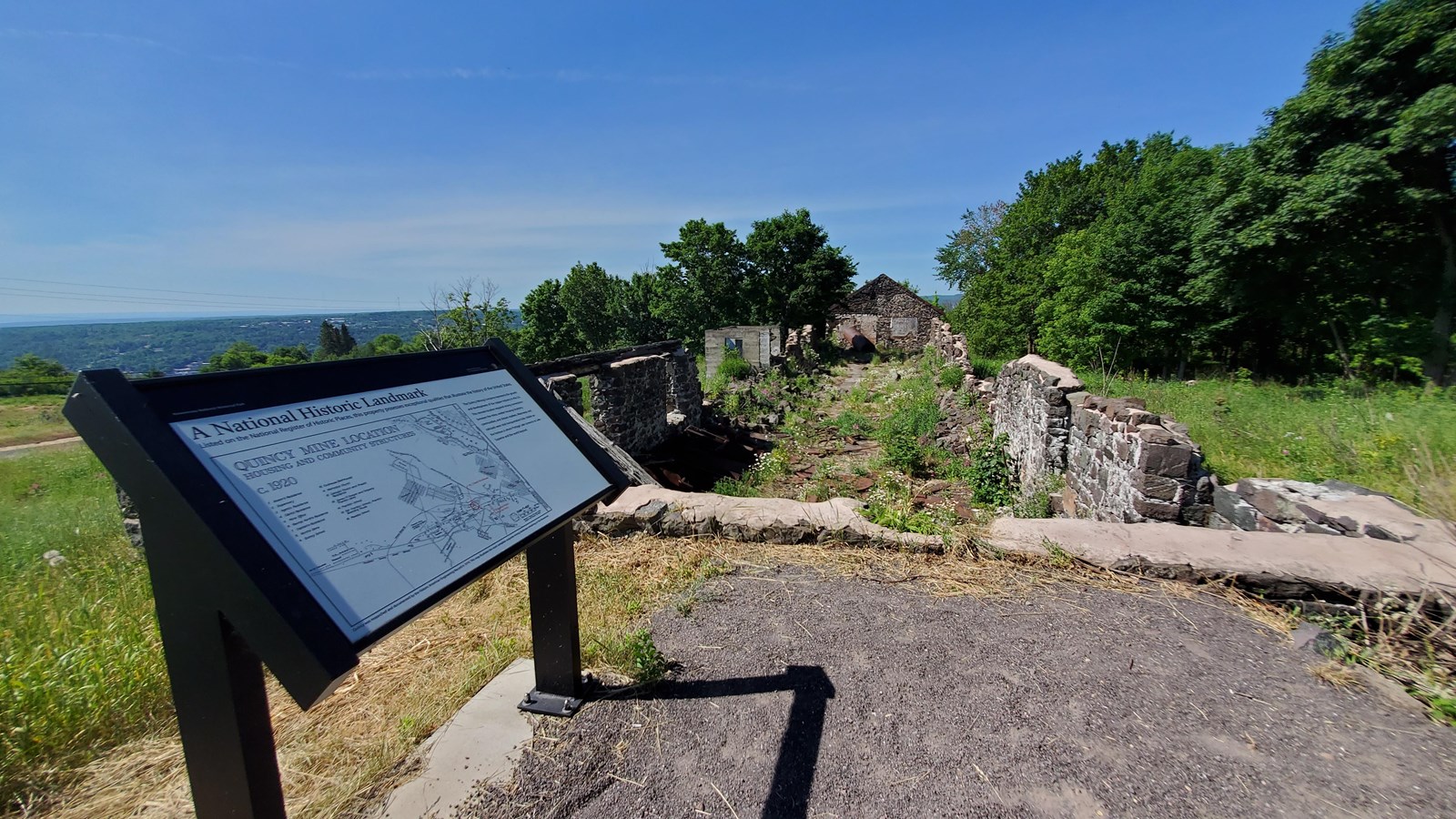 interpretive wayside is next to a gravel path with a long ruin foundation in the background