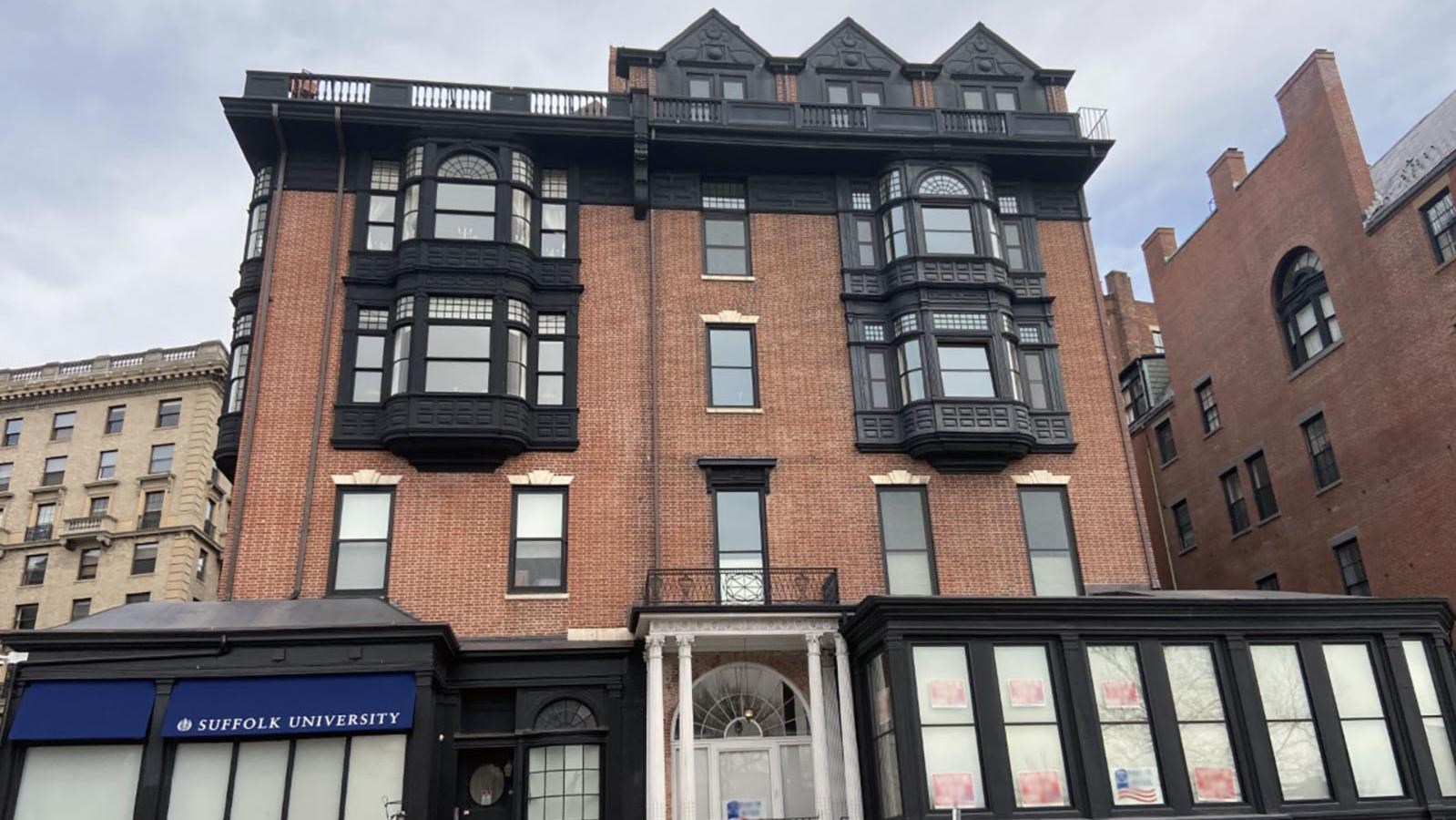 Brick building with black wood facade on 1st floor and black bay windows on upper floors.