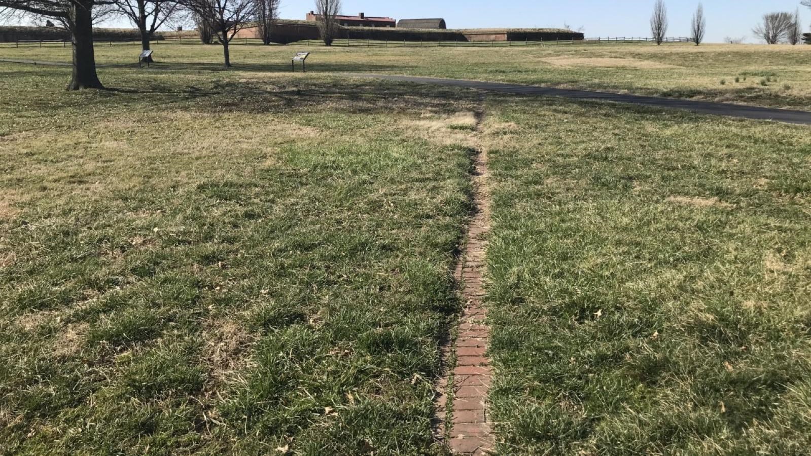 Brick foundation outlines facing towards the paved path leading to the fort.