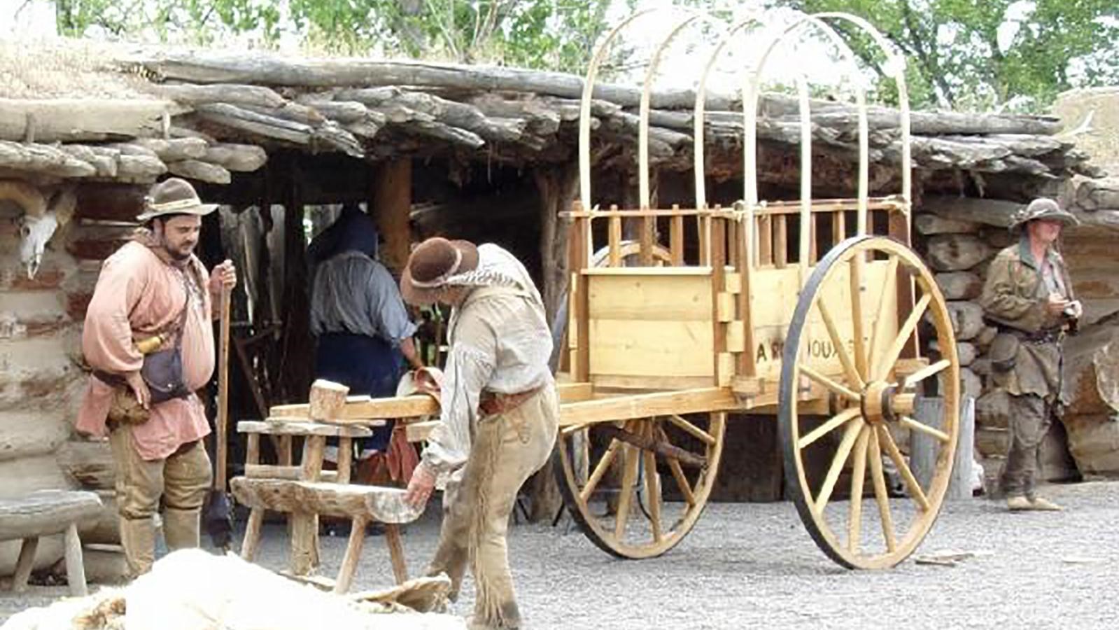 Two people in historic costumes stand outside an 18th century frontier fort.