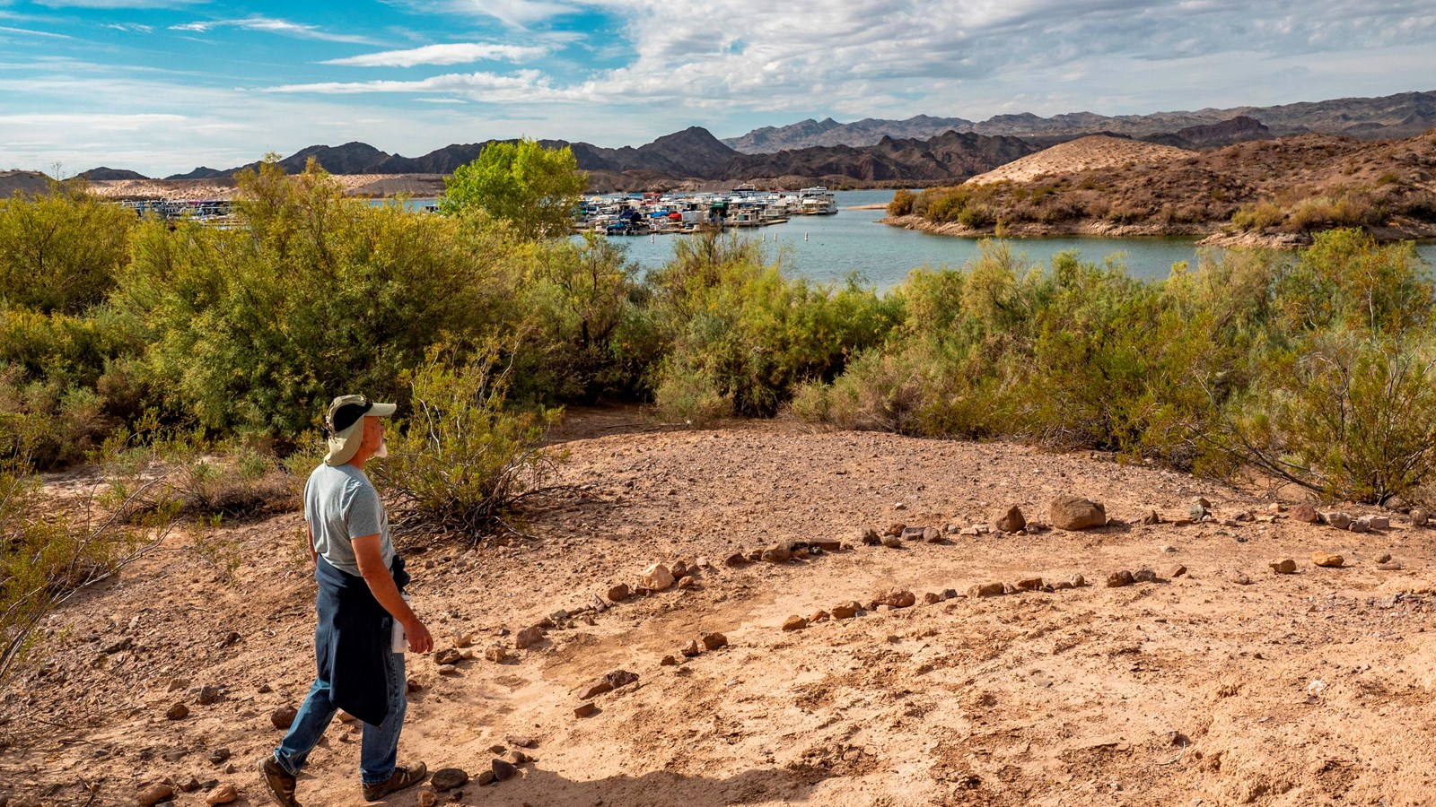 Man walking along a hiking trail with lake in the background.