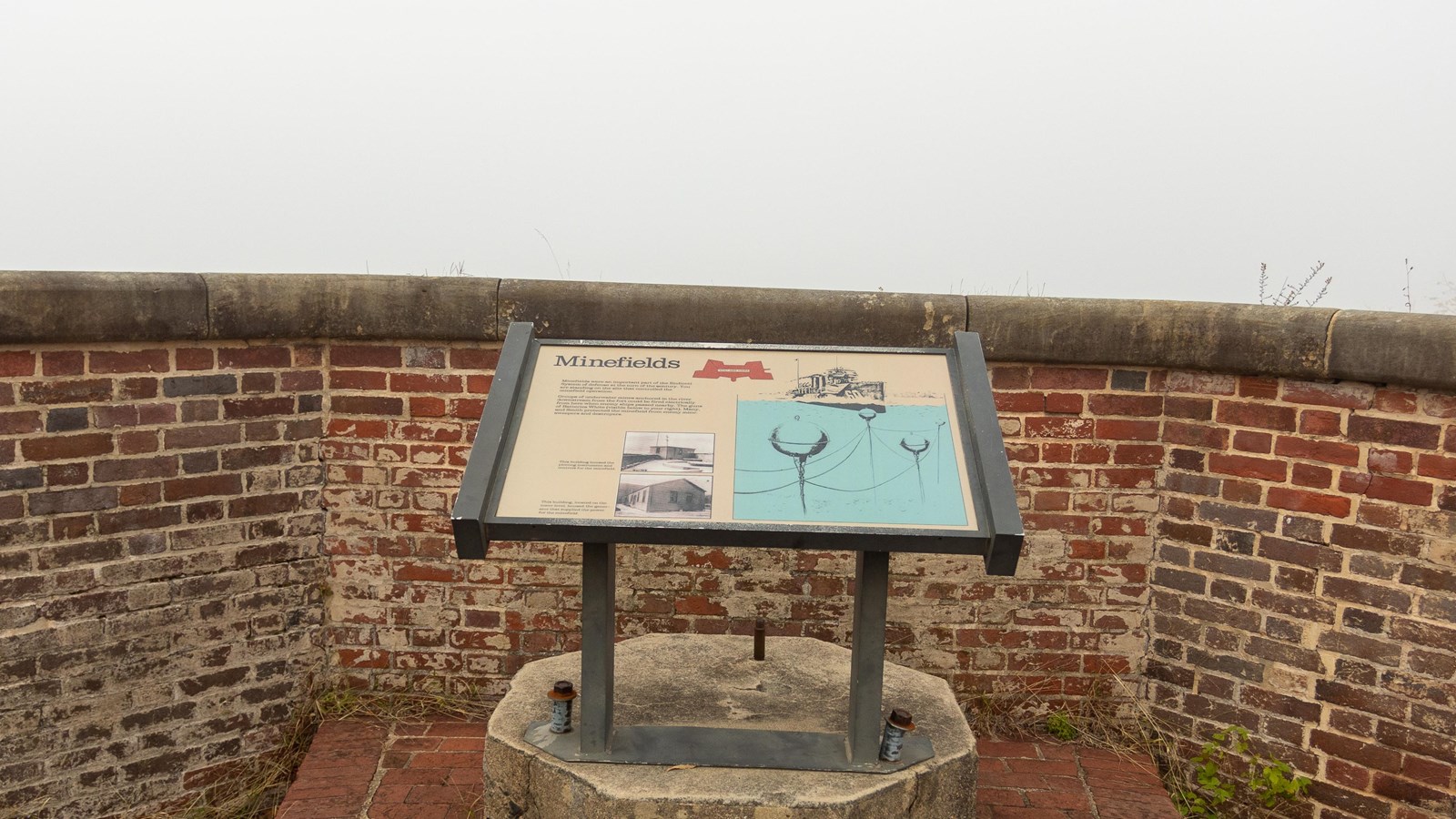 An interpretive-panel stands in front of a short, brick wall, featuring text, two photos, and a