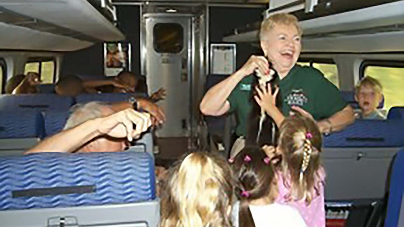 A woman in a green shirt holds up an animal pelt. Several people are gathered around looking at her.