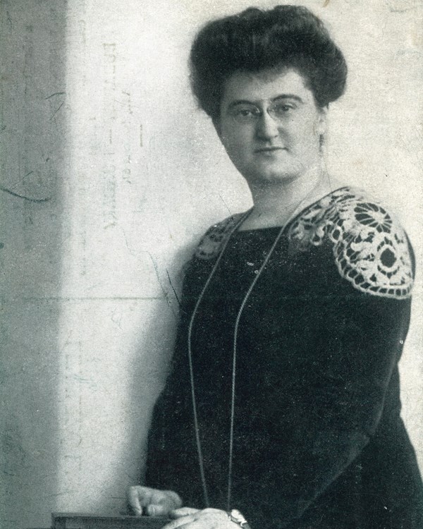 Woman standing with a stack of books, wearing glasses