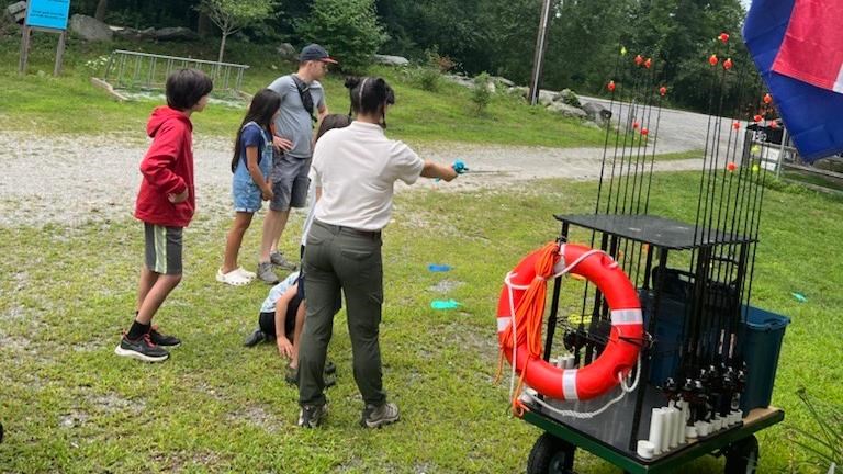 Intern demonstrates how to cast fishing rod to group of visitors