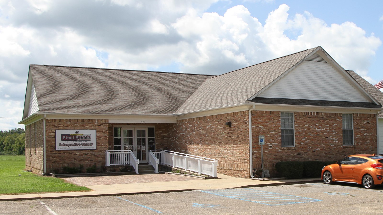 Brick building with an entry ramp on the left side. Ramp is white. Building borders parking lot.