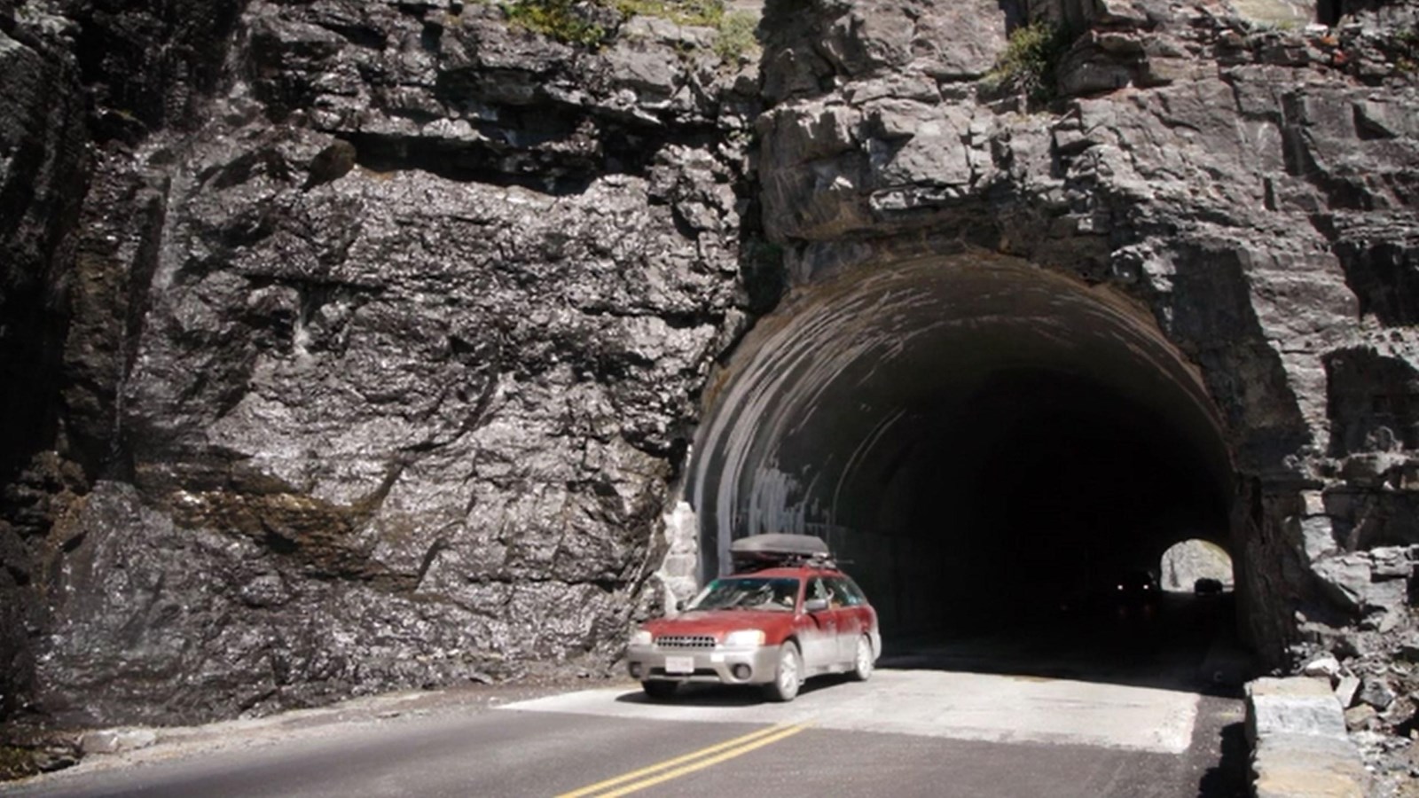 A car driving out of a tunnel carved into a mountainside.