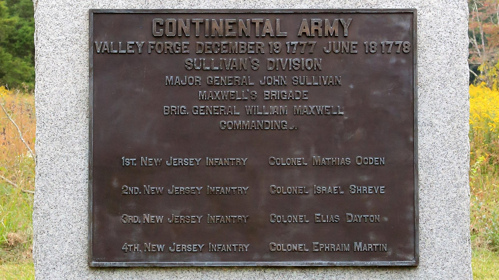 A large, smoothed granite block with a bronze plaque, sides and bottom are rough.