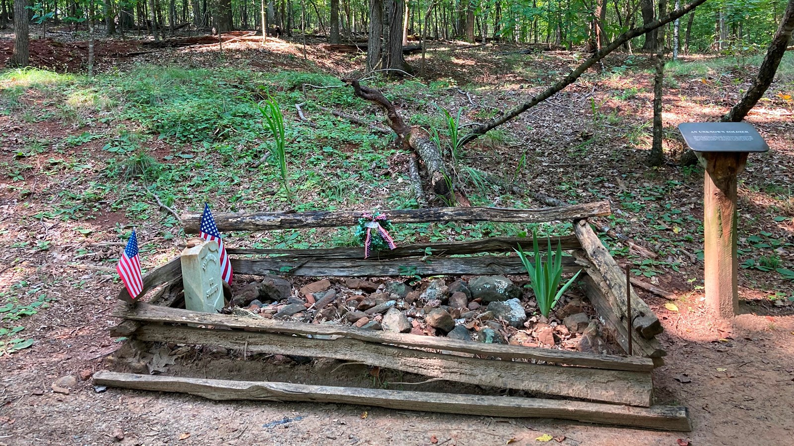 Picture shows a single gravesite. A marble headstone is surrounded by a small wooden fence.