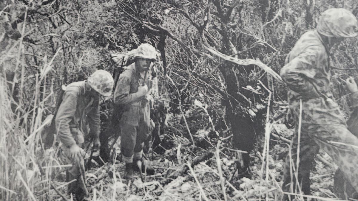3 tired Marines in helmets holding weapons take a break as they trek up the mountain.