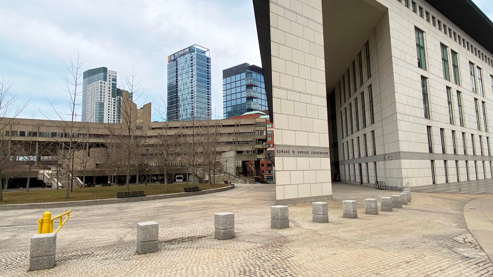 Corner of a modern white stone building that has a small plaza in front of it.