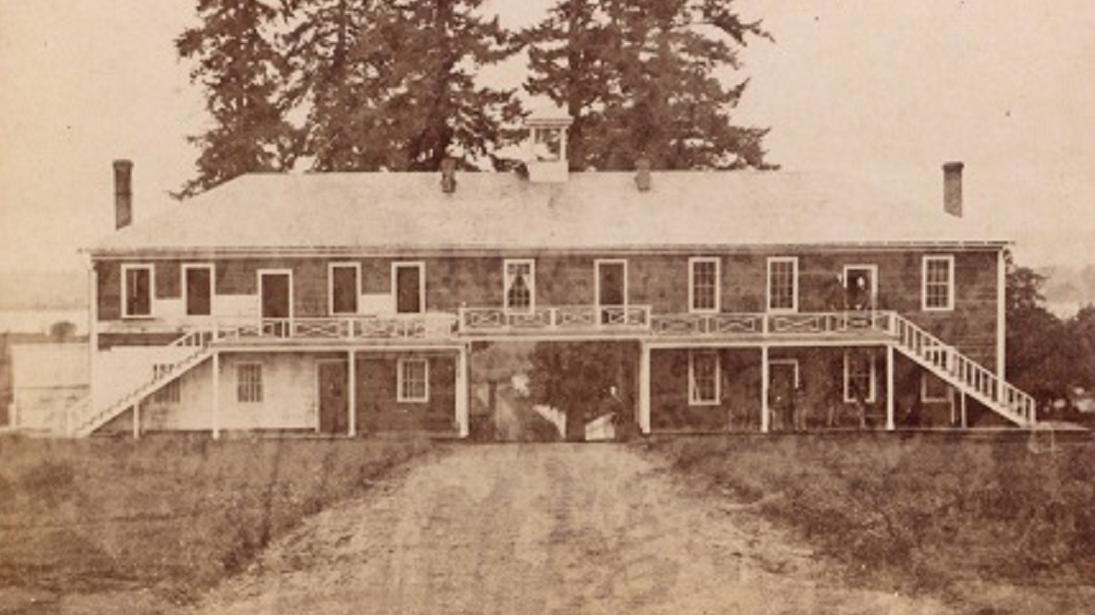 Black and white photo of a long two story building with a porch at its second level.